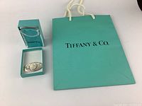 Photo of the Tiffany & Co. shopping bag, turquoise box with silver trimmed pouch, and the sterling silver oval bookmark featuring engraved world map design.