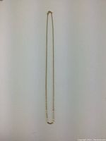 Full-length view of gold chain hung vertically on white background