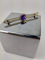 Front view of bar brooch showing oval purple amethyst set in yellow gold filigree
