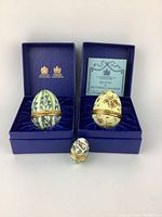 Photo of three enamel eggs in blue presentation boxes with certificates. One small egg placed in front.