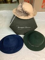 Three vintage wool felt hats arranged on a table with a green Georgena Spearn box in the background.