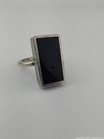 Side angle view showing rectangular black onyx stone set in sterling silver band, highlighting tiny divot in stone and silver texture.