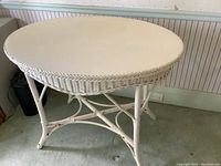 Front angled view of the vintage wicker oval table showing white painted wicker legs, cross supports and oval top.