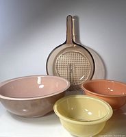 All three colourful Pyrex bowls and Corning Vision amber glass skillet arranged on white surface, showing colours and relative sizes
