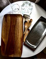 Full view of all items including wooden trays, wooden spoons, glass ladles, stainless steel trays and glass tealight warmer on a white round table.