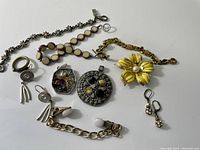 Overview of jewellery collection showing multiple bracelets, brooch, pendants and earrings arranged on a white surface.