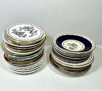 Two stacks of assorted orphan teacup saucers showing varying colors, floral patterns, and gold rim detailing.