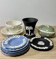 Top view showing all items in the collection: cup and saucer, vase, trinket box, blue and black plates, showing colors and white relief decoration.