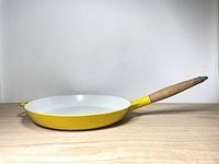 Side view of the yellow cast iron skillet with wooden handle on a wooden surface and white background