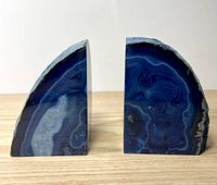 Front view of pair of blue agate geode bookends side by side showing polished surfaces with dark blue and black banding and natural rough edges.