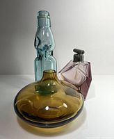 Front view of the three glass pieces showing form and color: amber Ikea vase, blue-green soda bottle, pink atomizer.