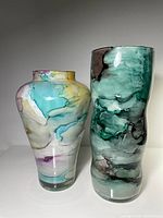 Two colorful glass vases by Franco; one rounded with multicolor watercolor patterns, one tall with green marbled pattern; glossy finish.