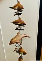 Full view of the vertical windchime with four brown ceramic dolphins mounted along with driftwood and shells, showing overall design and structure.