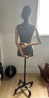 Full view of fabric body mannequin with wooden articulated arms on rolling legs in a room.