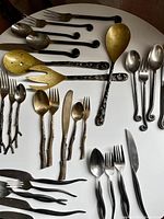 Full overhead view of mixed utensils laid out on white surface showing various materials, finishes, and forest inspired handles