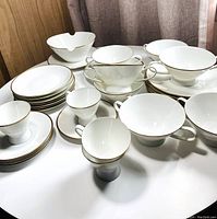 Image showing arranged porcelain cups, saucers, cream soup bowls, and gravy boat with white glaze and gold trim.