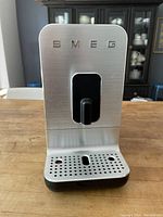 Front view of Smeg espresso machine showing stainless steel front panel, drip tray and integrated grinder outlet