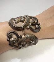 Bracelet worn on wrist showing size and design detail of silver bracelet with spiral and fan motifs and ball accents.