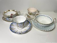 Four assorted teacups and saucers showing varied floral patterns and gold trim including Minton 'Vineyard' and Aynsley cups.