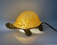 Side view of turtle lamp lit, showing warm mottled glass shell and brass turtle body with head and legs visible.