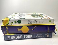 Side view of three stacked cookbooks focusing on vegetable and vegan cooking, showing the titles and authors on the spines.