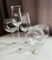 Photo showing 5 different Moser snifter glasses of unique shapes on white surface against brown curtain background.