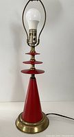 Full view of vintage red and brass table lamp with red conical base and brass accents, light bulb installed but no shade, power cord visible.