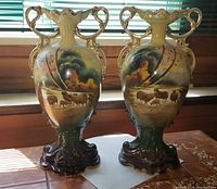 Pair of large antique American vases with pastoral handpainted scenes, ornate handles, and scalloped rims, placed on tiled surface.