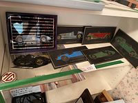 Five rectangular car plaques displayed on a shelf showing different vintage race cars with mirrored finish and black backgrounds.
