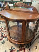 Full view of half round wood and glass display cabinet showing curved glass front and carved wood detail on top.
