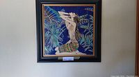 Framed ceramic tile artwork showing full image of a kneeling woman with arms raised against a blue crackle floral background.