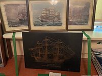 Three framed sailing ship pictures arranged in a row behind the black plastic copper-colored ship artwork.