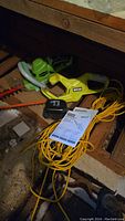 Full view of two hedge trimmers, battery charger, long yellow extension cord, and instruction manuals on floor.