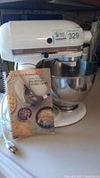 Front view of white KitchenAid Ultra Power mixer with stainless steel bowl attached and manual booklet leaning against bowl showing brand and recipe/instruction title.