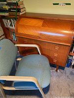 Angle view of teak roll-top desk next to teal upholstered side chair