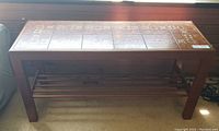 Full view of the rectangular oak sofa/display table with brown decorative tile top and open shelf below.