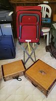 Front view of red Swiss Gear spinner luggage with vintage brown suitcases on floor