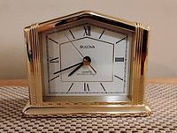 Front view of brass Bulova mantle clock with white dial, Roman numerals and black hands inside a glass face cover.