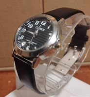 Close-up photo of the Caprice wristwatch showing the black dial, silver case, and leather strap.