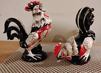 Set of four ceramic rooster figurines painted in red, black, and white colors, arranged on a textured mat; all approximately 5 inches tall each.