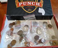 Top view of cigar box containing multiple small plastic bags with assorted coins, showing various sizes and types of coins inside.