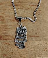 Necklace with detailed silver-tone owl pendant on a box chain laid on wood surface.