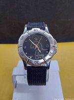 Front view of men's dive style wristwatch with black fabric strap and silver-tone bezel, showing dial details and hands.