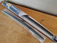 Photo shows a pair of windshield wiper blades on a wooden surface, one packaged in branded Michelin Stealth packaging (24 inch), the other sealed in clear plastic (20 inch).