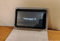 Tablet screen powered on showing 'Voyager III' startup logo inside gray fabric cover.