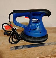 Front and side views of the blue Simoniz orbital polisher with 8 inch polishing area and electric cord coiled beside it, ruler placed in front for scale.