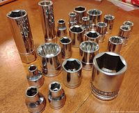 Photo showing 20 chrome-finished 3/8 inch drive sockets in assorted sizes arranged on wood surface.
