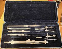 Open view of the case showing several brass technical drafting instruments mounted in black velvet lining.
