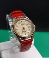 Front and angled view of vintage women's Zeon wristwatch with red leather strap, white dial, gold-tone hands and markers, fluted gold bezel, and date window at 3 o'clock position.