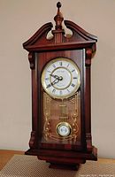 Front view of the Westminster chime pendulum wall clock showing the clock face, Roman numerals, hands, and pendulum behind decorative glass.